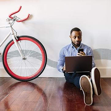 man with a phone and computer sitting next to a bicycle